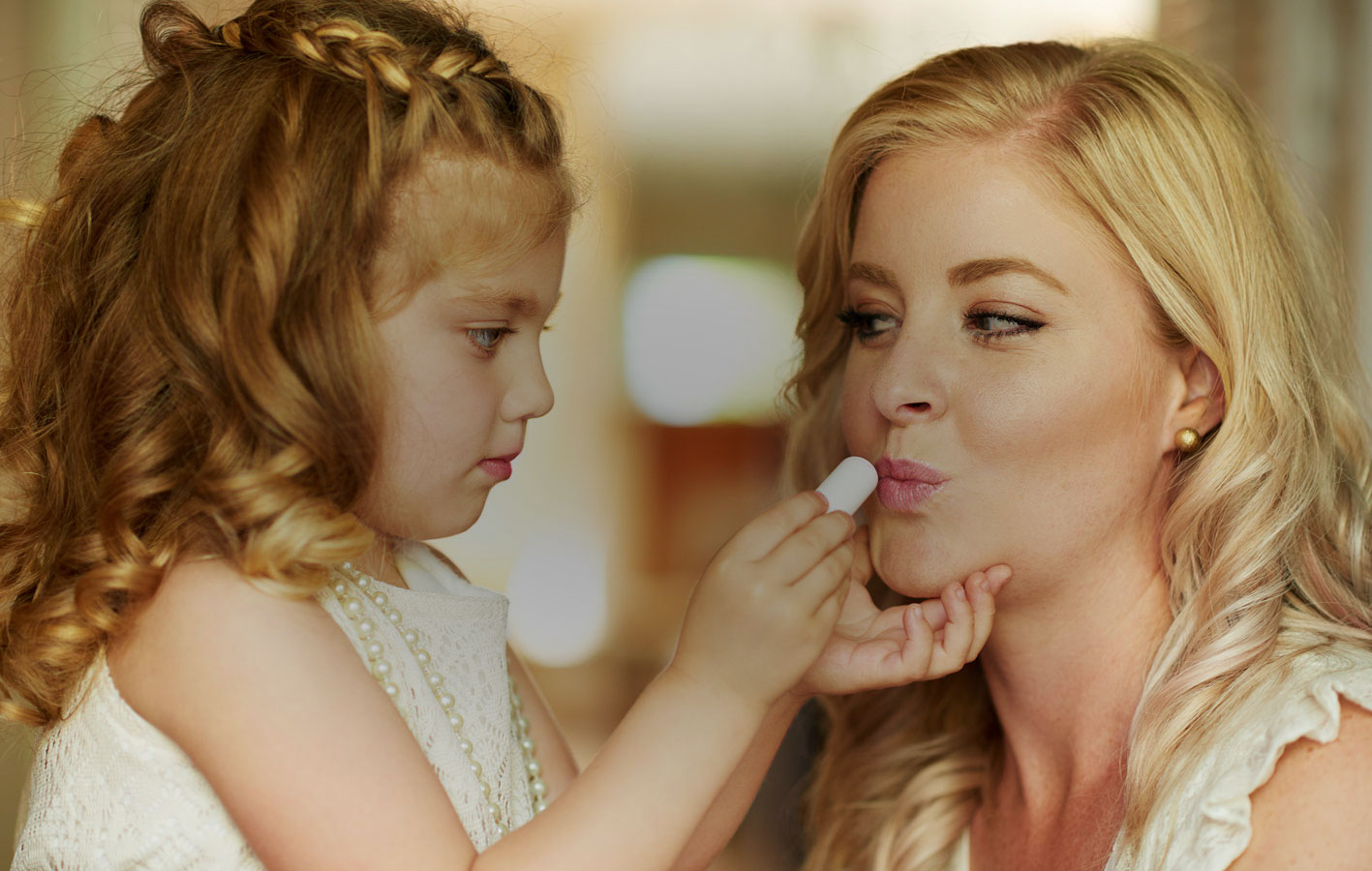 Little girl putting lip-gloss on Mom
