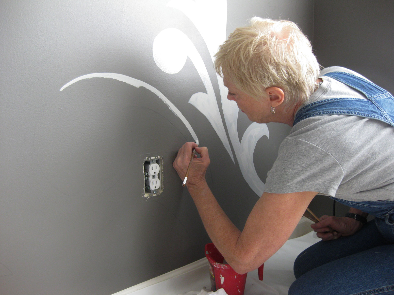 Woman using brush to paint mural by electric outlet
