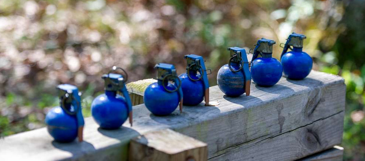 blue training grenades lined up on a stack of railroad ties